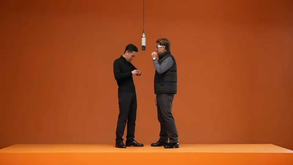 Two performers on an orange stage beside one hanging microphone